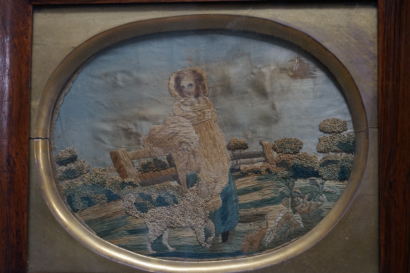 A pair of early 19th century rosewood-framed silk worked oval embroideries. Each embroidered with a boy and girl in a country landscape with their dogs. Worked in stem stitch and a knotting, the sky and faces hand painte